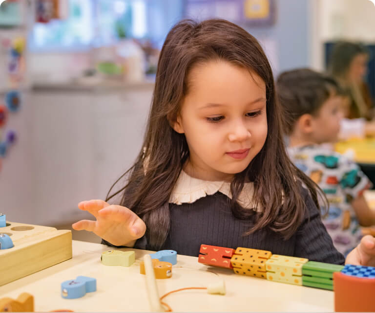 A preschool girl plays with colorful wooden counting blocks at a classroom table.